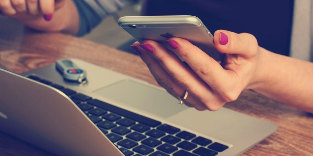 woman with fuchsia painted nails at desk in front of laptop holding an iPhone