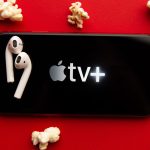 apple tv+ logo on mobile screen with popcorn and earbuds surrounding