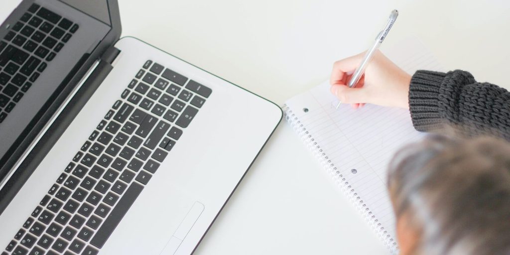 person writing on a notepad next to the computer